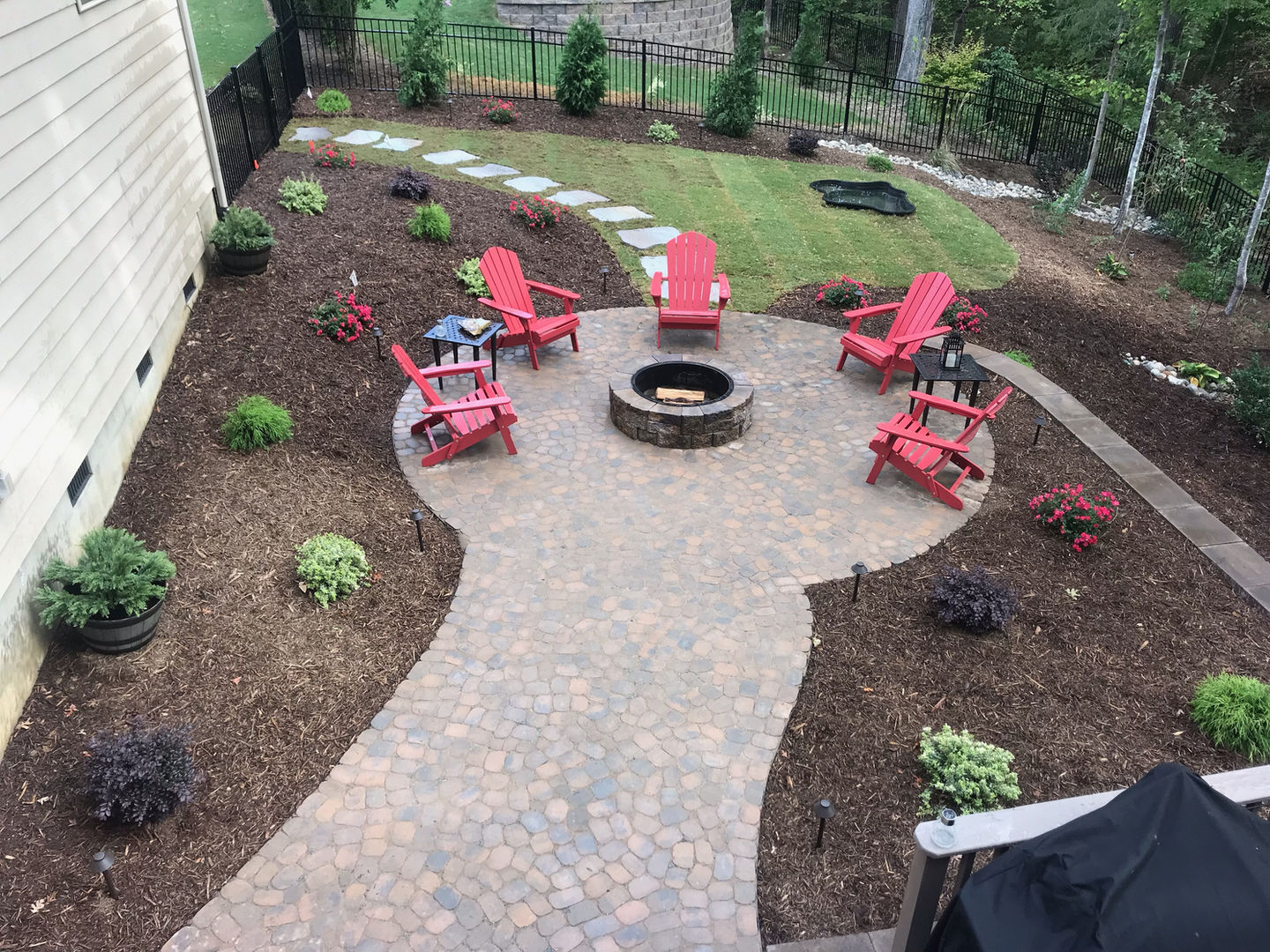 Handcrafted outdoor fire pit on a stone patio with red chairs.