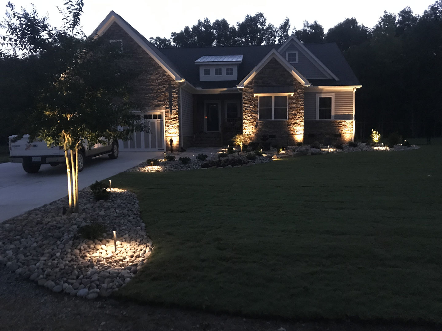Illuminated driveway and lawn at night with house lights.