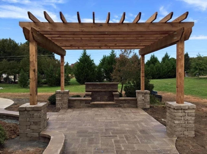 Wooden pergola on stone pillars over a paved patio.