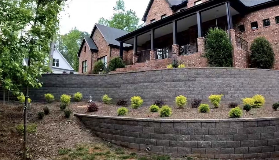 Tiered stone retaining walls with landscaping outside a brick home